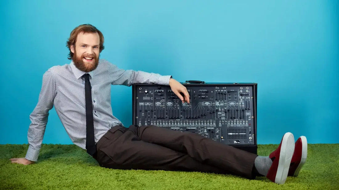 Todd Terje seated beside a synthesiser against a blue background