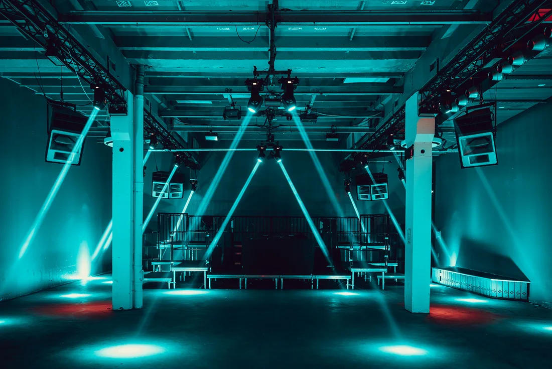 DSTRKT empty club room with teal light beams, steel columns, stage