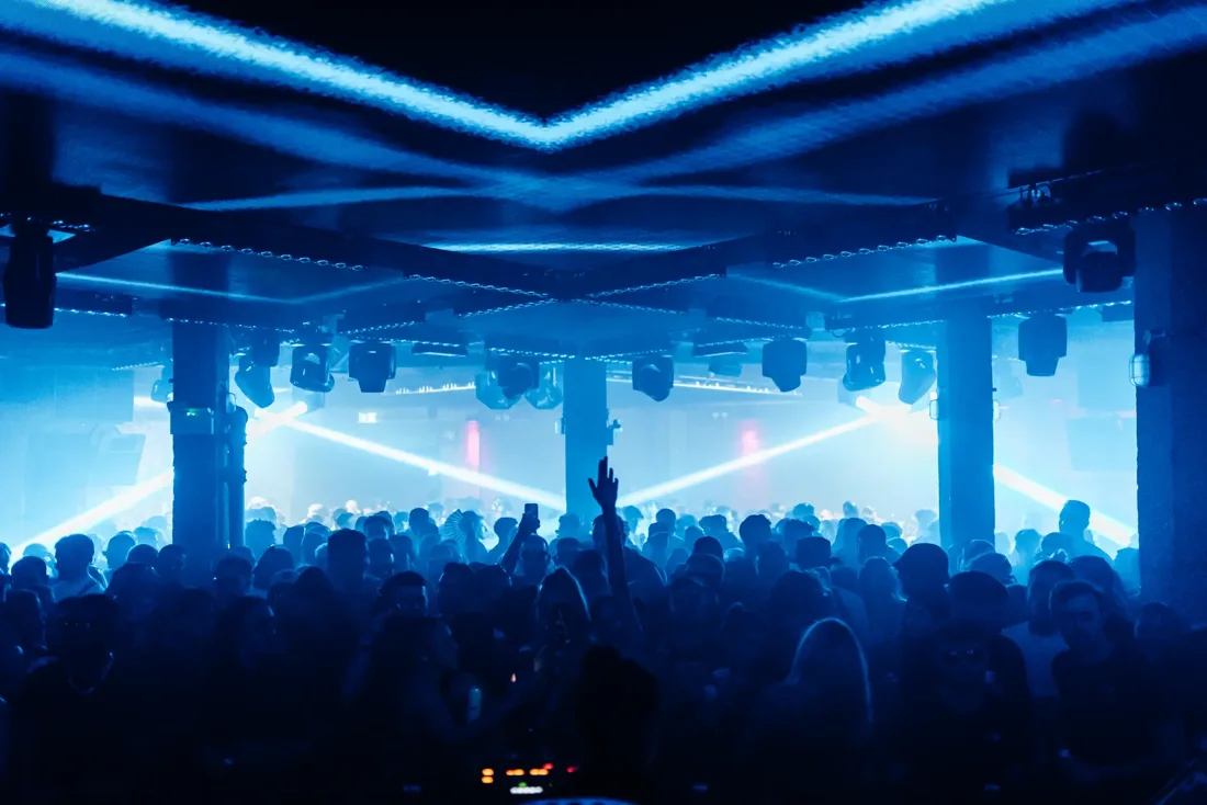 E1 packed dancefloor under blue light rig, pillars and low ceiling
