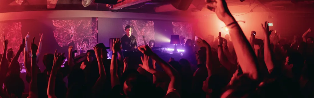 A DJ performing for a raised-hands dancefloor crowd at MDLR Singapore