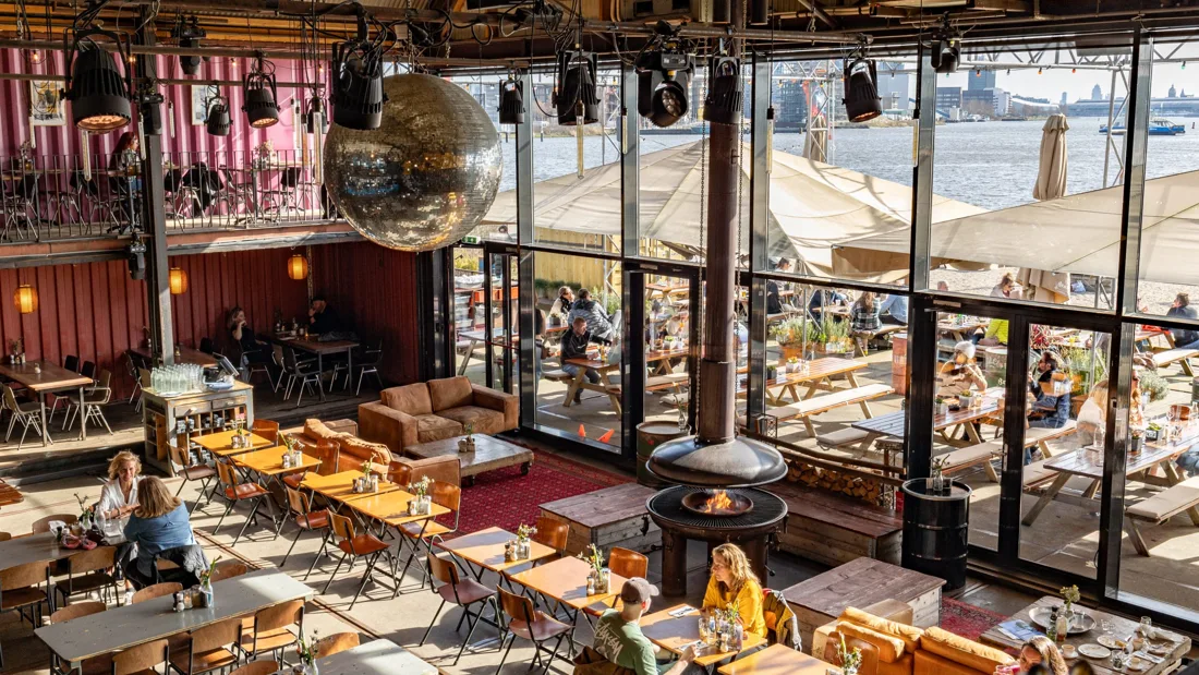 Pllek restaurant hall with disco ball, fire pit and glass wall onto the IJ