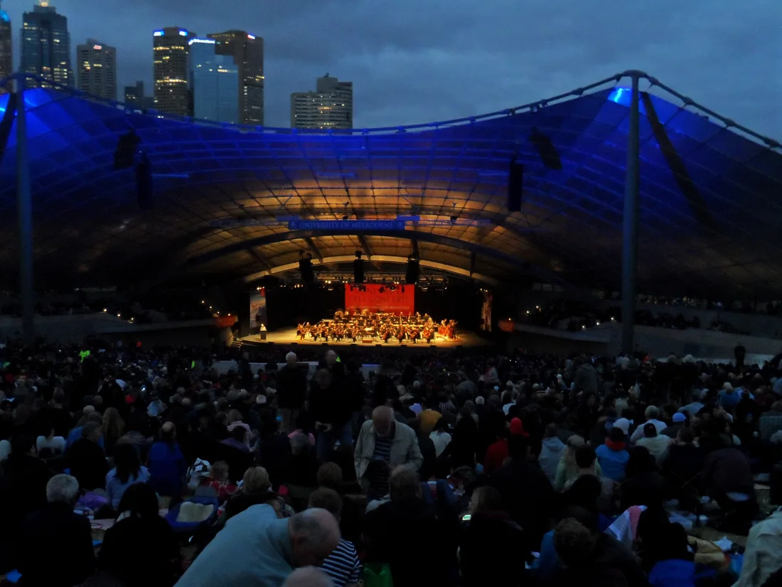 Sidney Myer Music Bowl blue-lit canopy over a dusk concert and city skyline