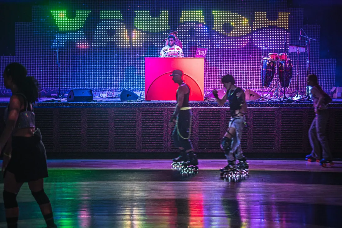 Xanadu roller rink with skaters, stage and DJ booth before LED wall